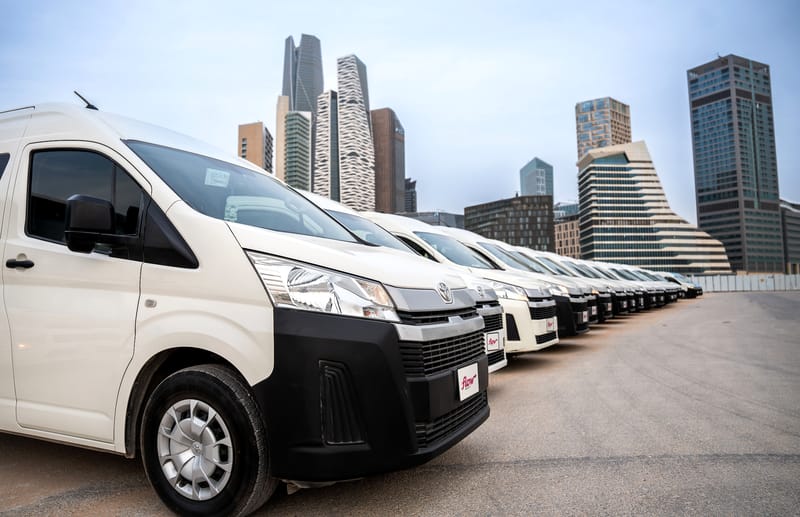 A long row of white Flow Mobility Toyota Hiace buses in Riyadh